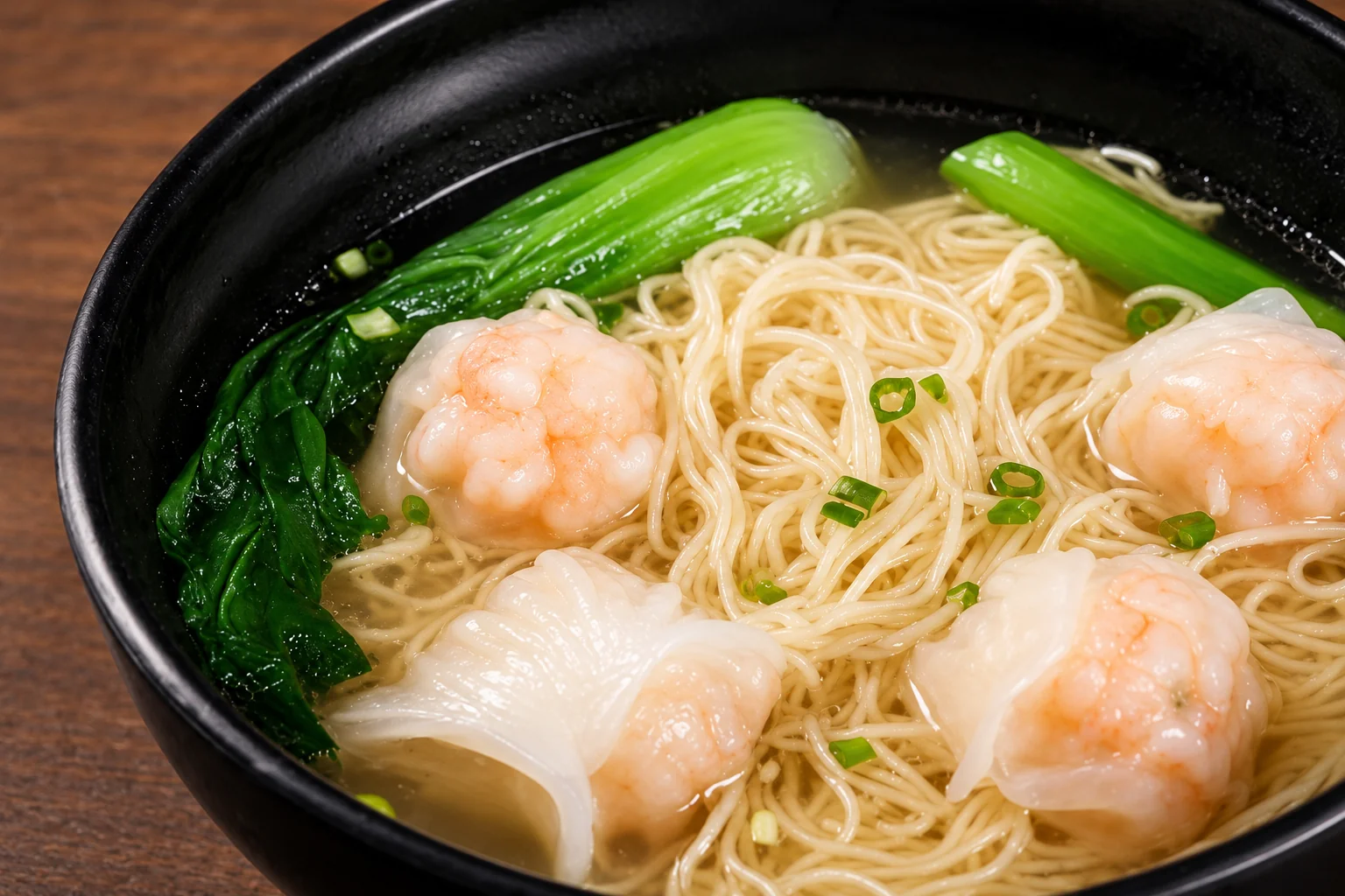 Bol noir de nouilles fines en bouillon clair, avec des raviolis de crevettes, du pak-choï et de la ciboule.
